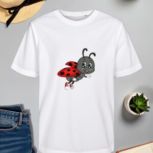Bijela majica s ilustracijom vesele bubamare s crvenim krilima i crnim točkicama, koja nosi crvene tenisice i leti s osmijehom na licu. Majica je položena na ravnu površinu uz slameni šešir s crnom vrpcom, svijeću, zelenu biljku u tegli, otvorenu knjigu i traperice.