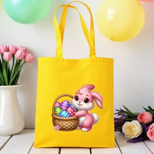 žuta platnena vrećica s motivom preslatkog rozog zeca koji drži košaricu punu šarenih pisanica. Vrećica je postavljena na drveni stol, okružena pastelno obojenim balonima i cvijećem u pozadini.